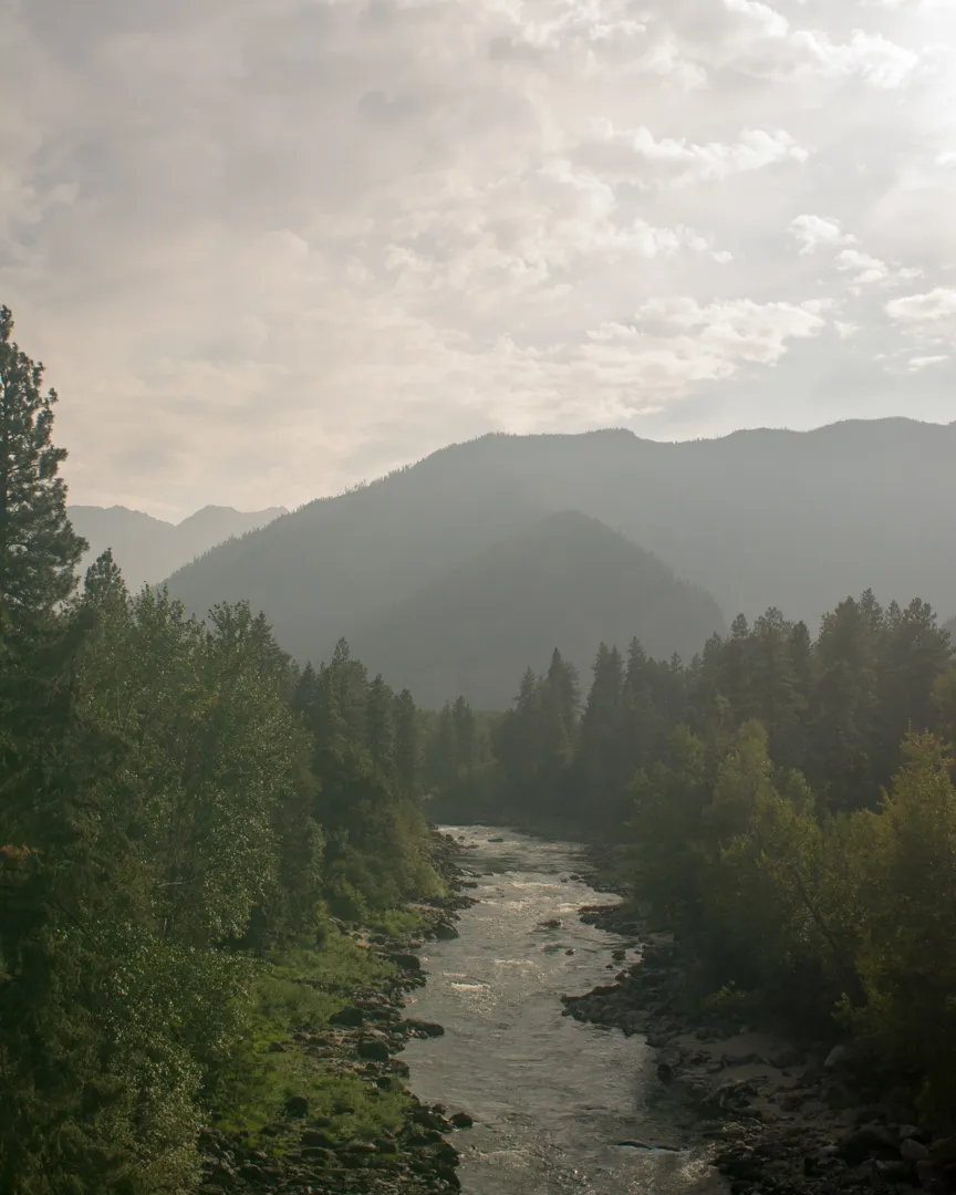 A mountain river valley near Leavenworth, Washington, with the Wenatchee River winding through dense conifers under a smoke-hazed sky during wildfire season
