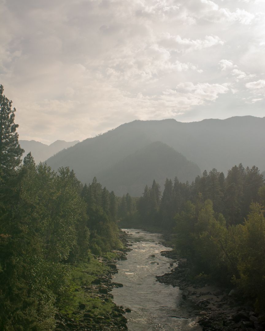A mountain river valley near Leavenworth, Washington, with the Wenatchee River winding through dense conifers under a smoke-hazed sky during wildfire season